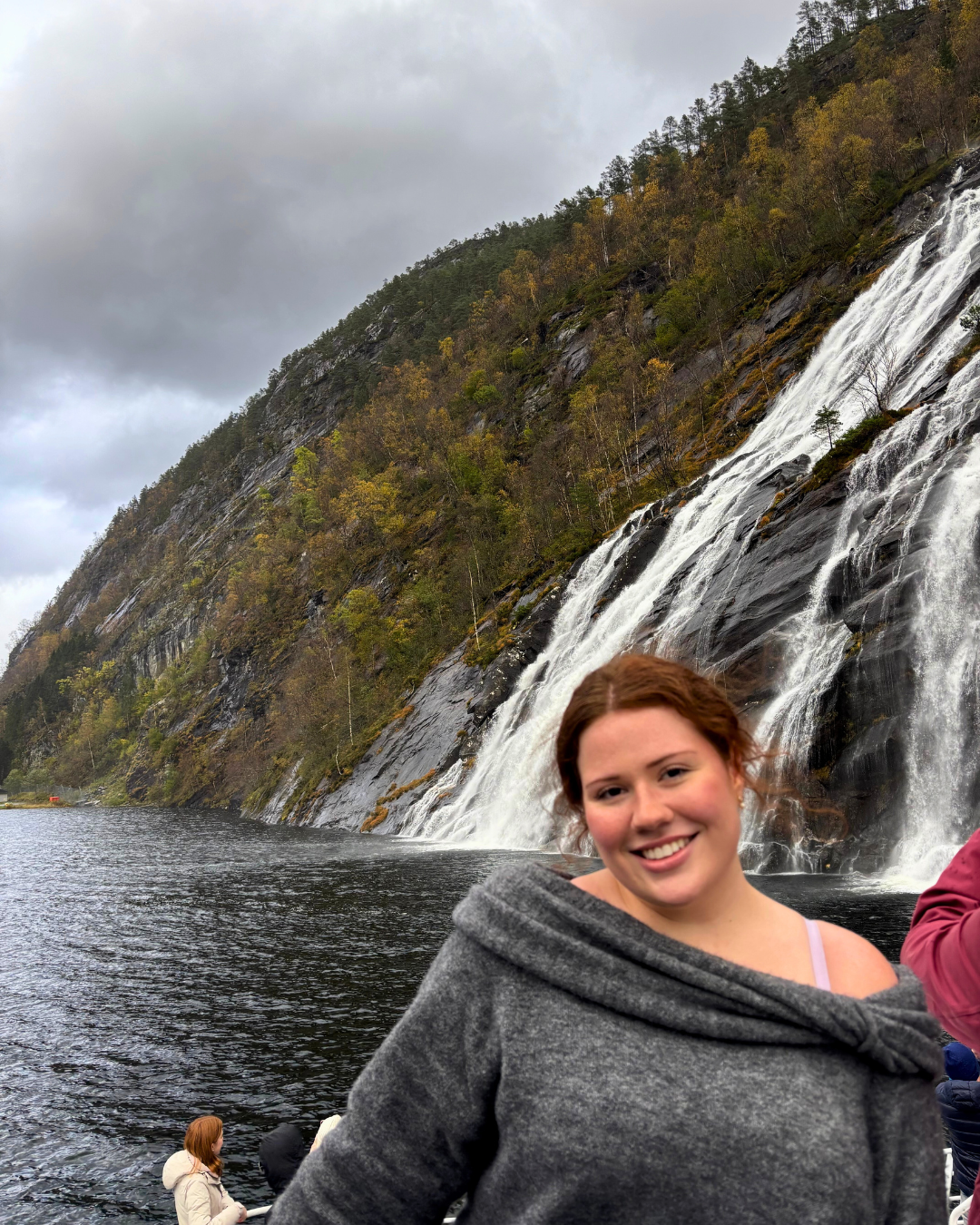 Ava smiles in front a massive watefall from a boat on a cloudy day