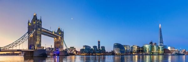 Panoramic view of a cityscape at dusk with Tower Bridge and modern skyscrapers, including the Shard.