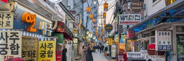 A busy street in an urban area with colorful signs in Korean and paper lanterns hanging above.
