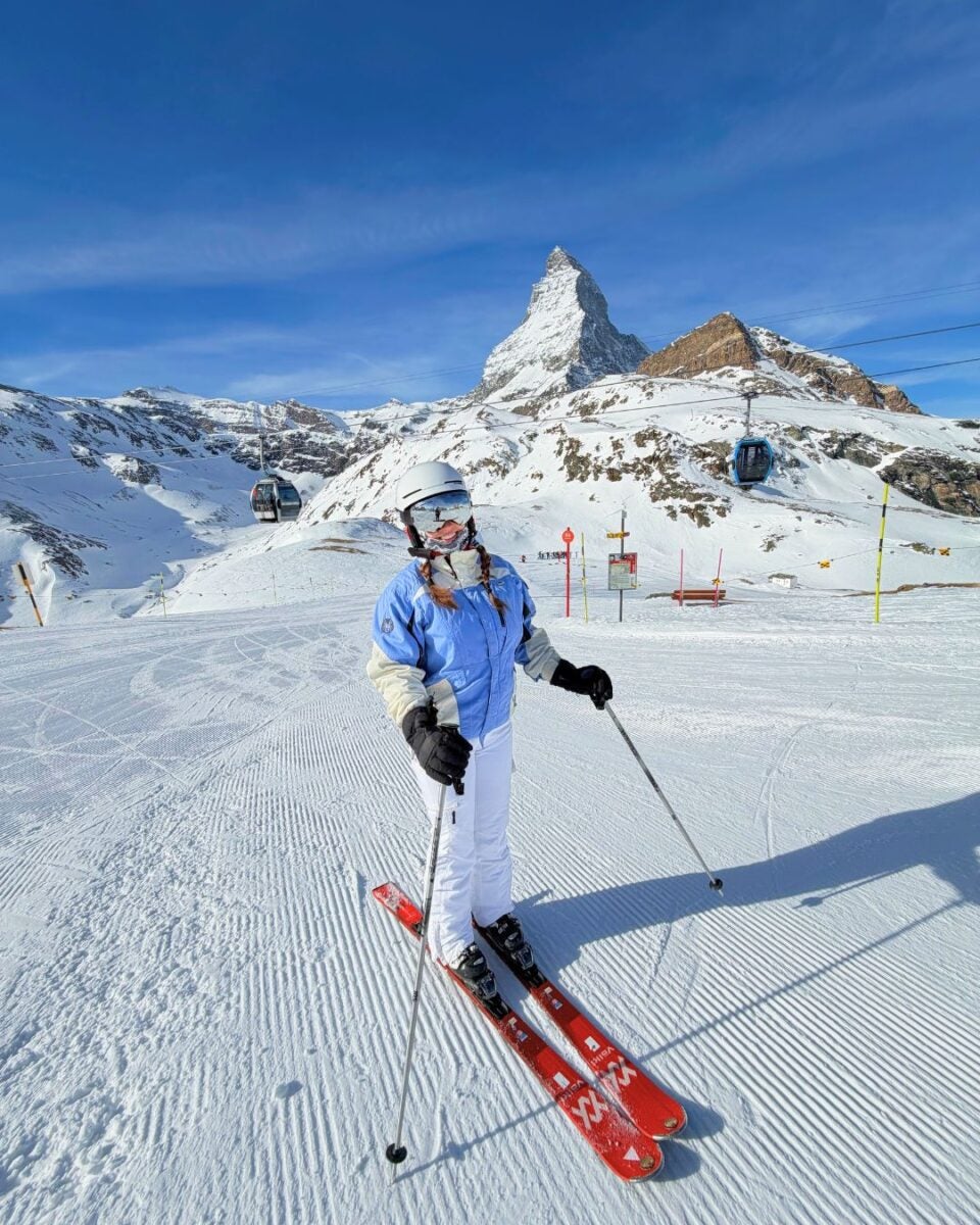 Skier on a snowy slope with the Matterhorn and ski lifts in the background.