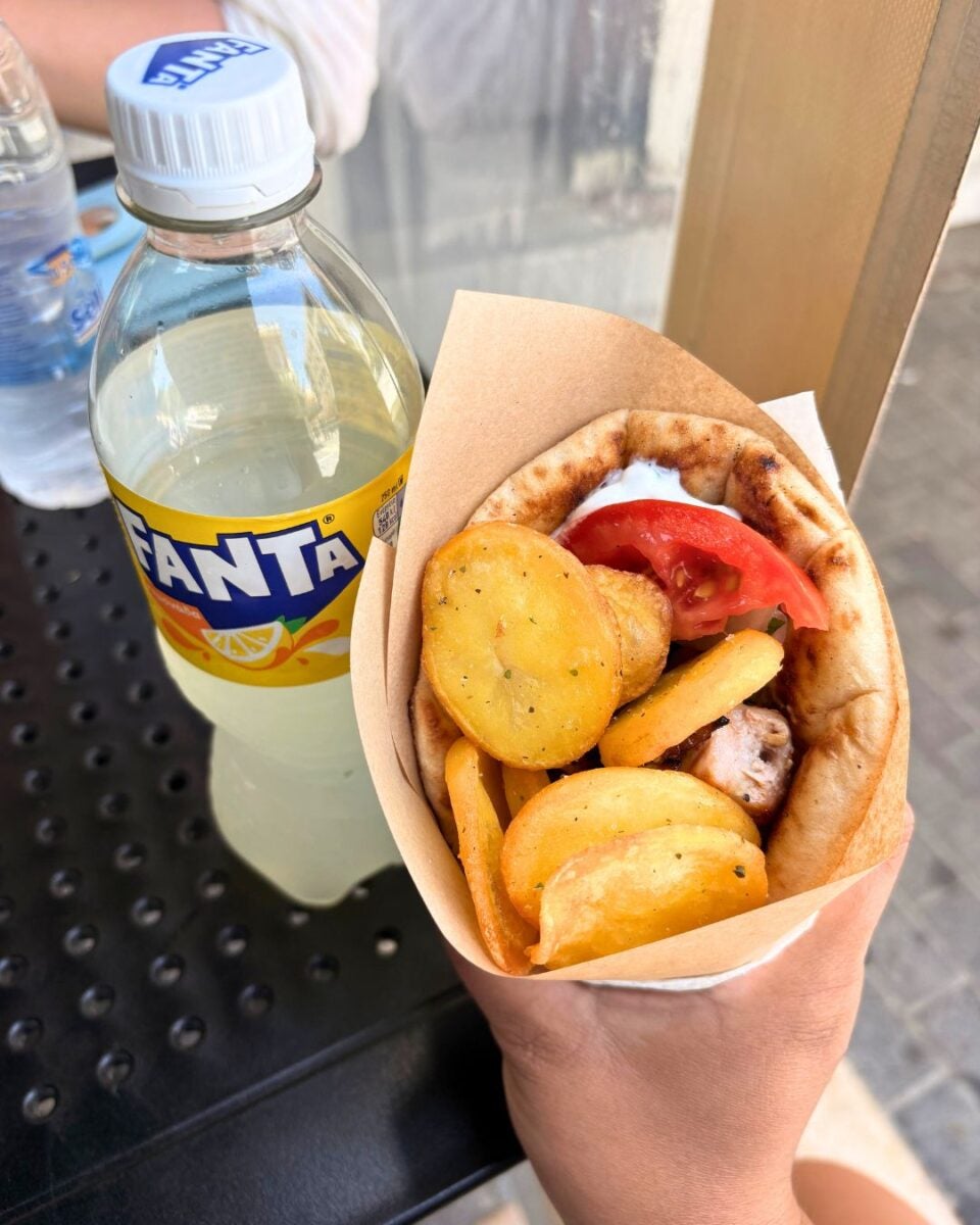 A gyro filled with meat, tomato, and fried potato slices next to a bottle of Fanta lemon soda.