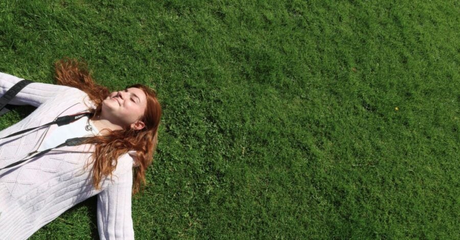 A woman with red hair lying on green grass, wearing a white sweater.
