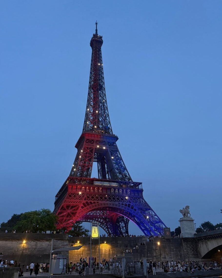Eiffel Tower illuminated in red, white, and blue lights against a clear evening sky in Paris.