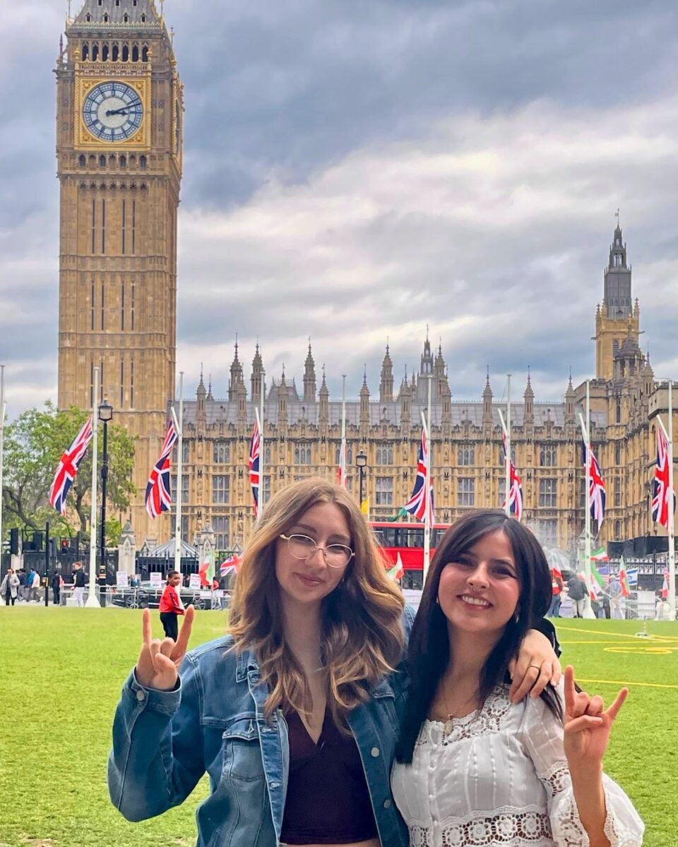 Two woman smiling in front of a historic building with Union Jack flags.