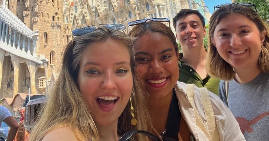 Four smiling friends take a selfie in front of the intricate facade of Sagrada Família. Bright, sunny day conveys joy and excitement in Barcelona.
