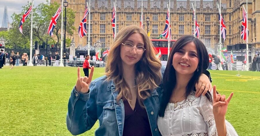 Two woman smiling in front of a historic building with Union Jack flags.