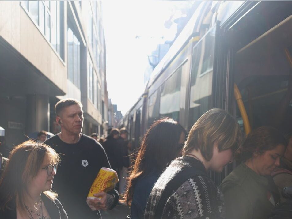 Crowded urban street scene with people boarding a bus on a sunny day between tall buildings.