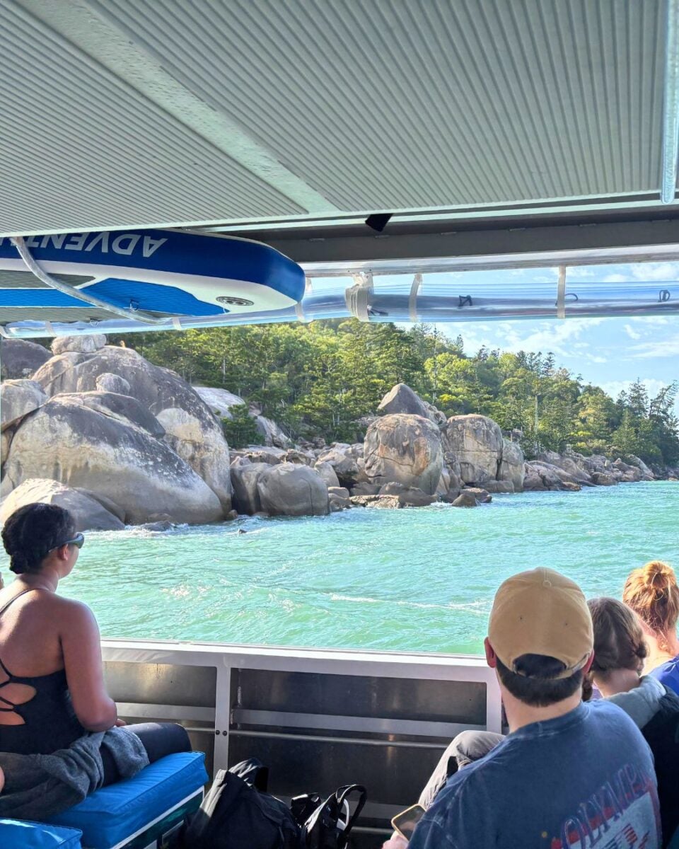 Passengers on a boat viewing a rocky shoreline and turquoise water.