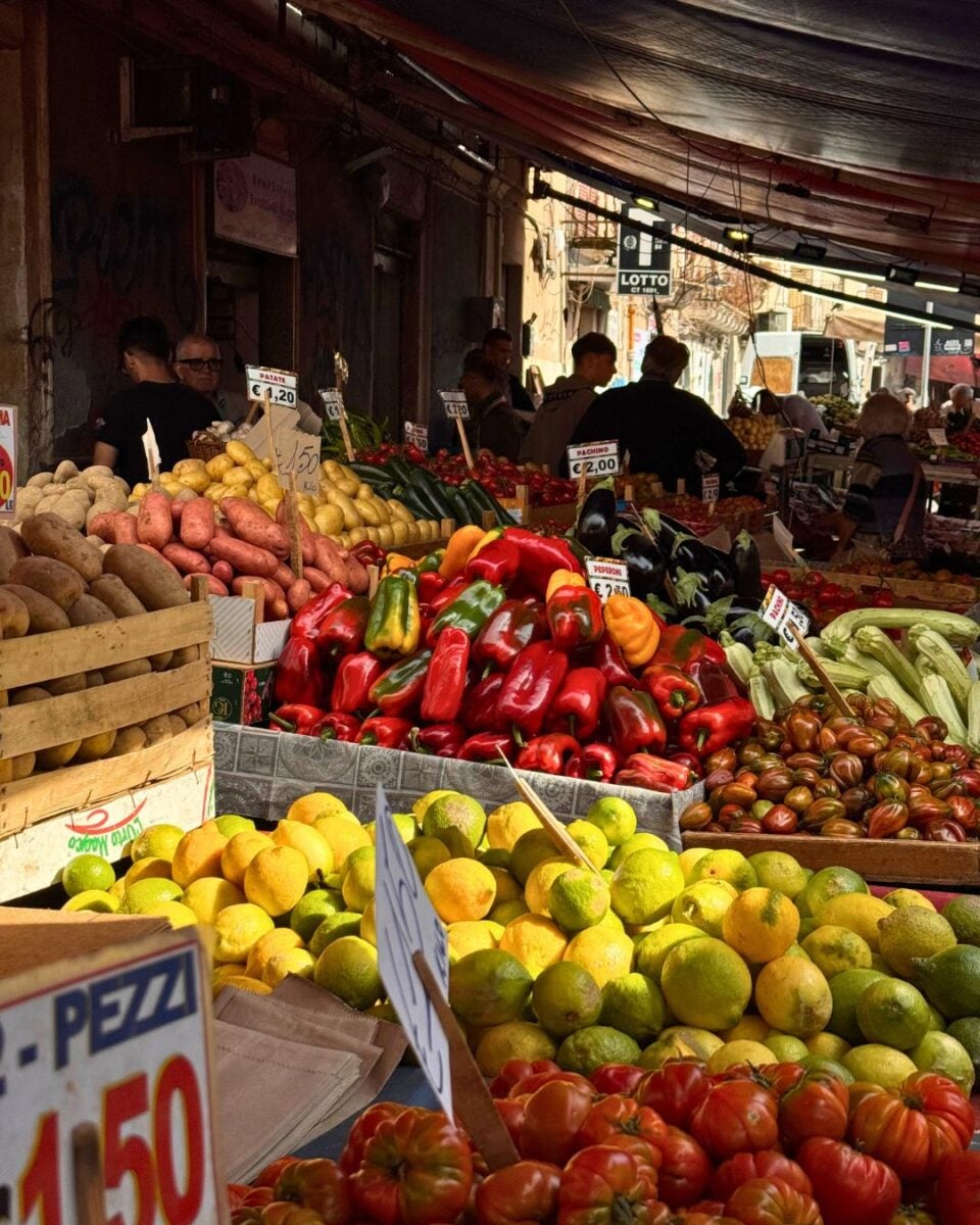 Vibrant market scene showcasing a variety of fresh fruits and vegetables, including peppers, tomatoes, and lemons, with price tags visible.