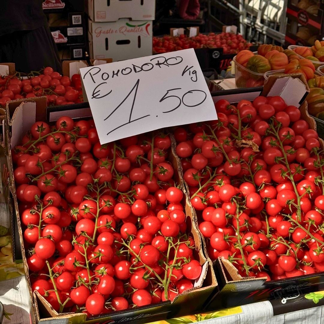 Fresh red cherry tomatoes displayed in a market with a price sign indicating €1.50 per kilogram, highlighting local produce.
