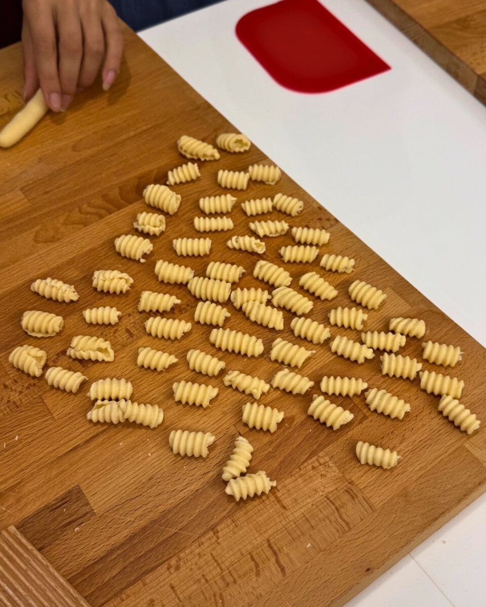 Freshly made ridged pasta on a wooden surface with a hand shaping dough.
