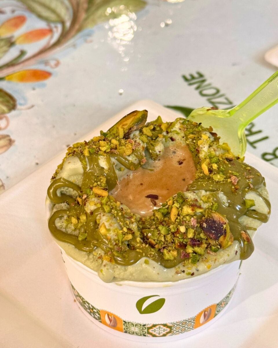 Gelato with pistachio toppings in a patterned cup with a green spoon.
