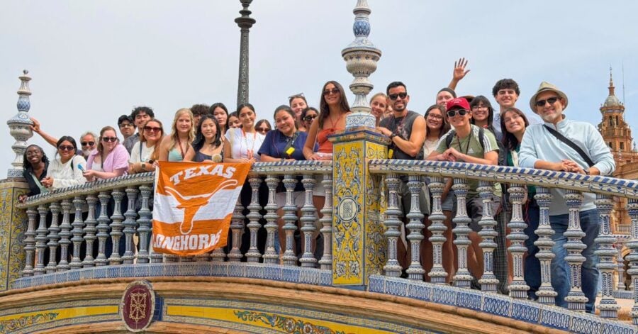 A group of people on an ornate tiled bridge holding a Texas Longhorns flag.