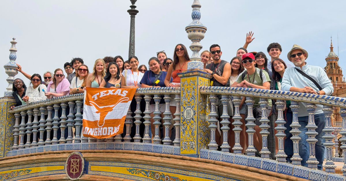 A group of people on an ornate tiled bridge holding a Texas Longhorns flag.