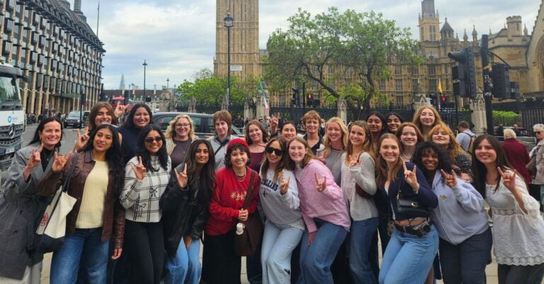 Group of diverse young women posing happily in front of Big Ben and the Houses of Parliament in London on a cloudy day.