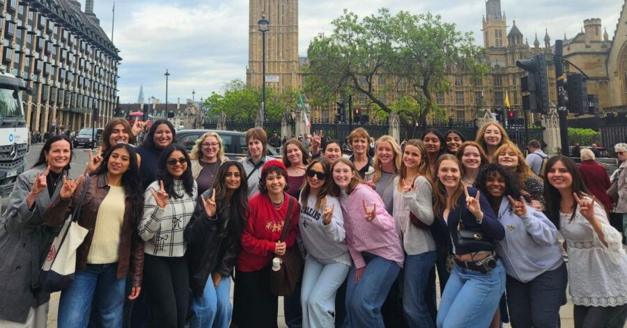 Group of diverse young women posing happily in front of Big Ben and the Houses of Parliament in London on a cloudy day.