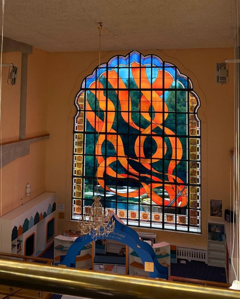A large stained glass window featuring intricate designs, illuminating the interior of a historic building.