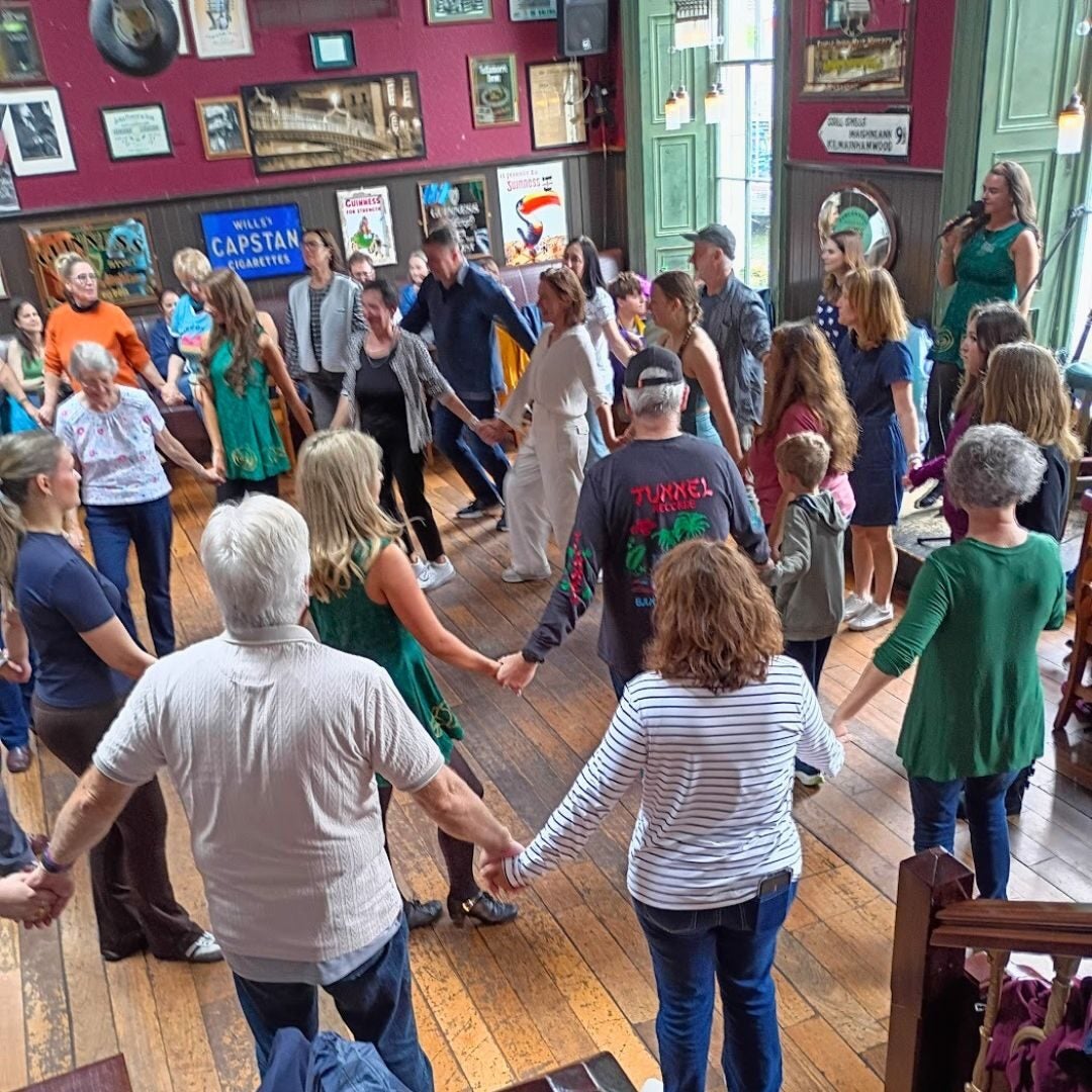 A diverse group of people holding hands in a circle inside a cozy room with wooden floors and vintage posters on the walls.