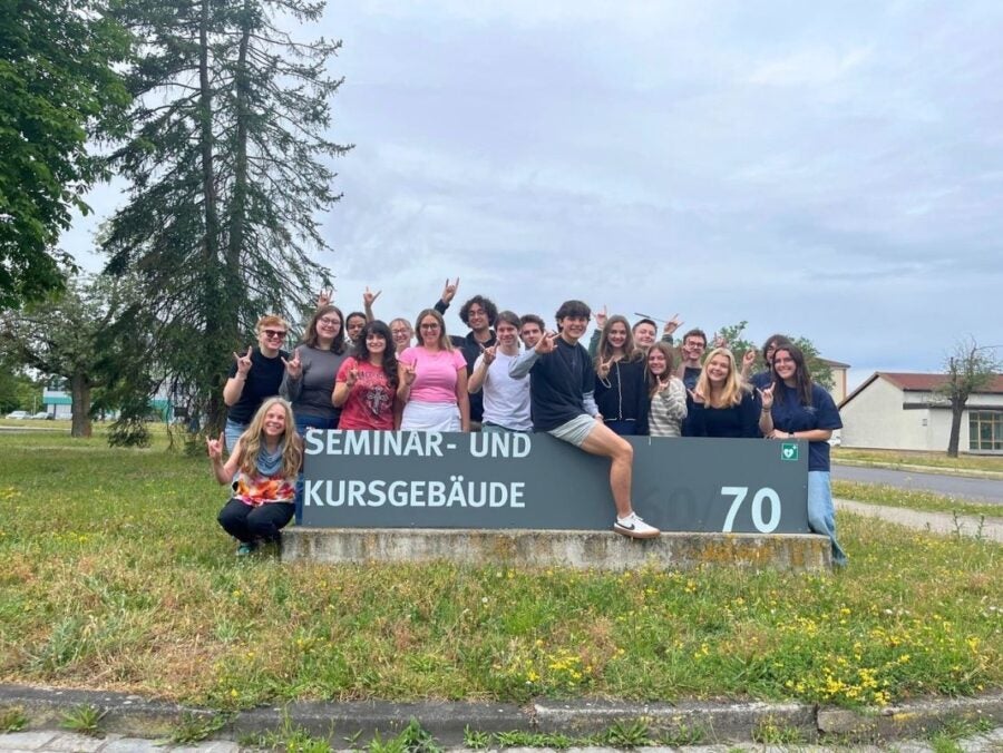Group of young people posing happily around a Seminar and Course Building sign outdoors on a cloudy day.