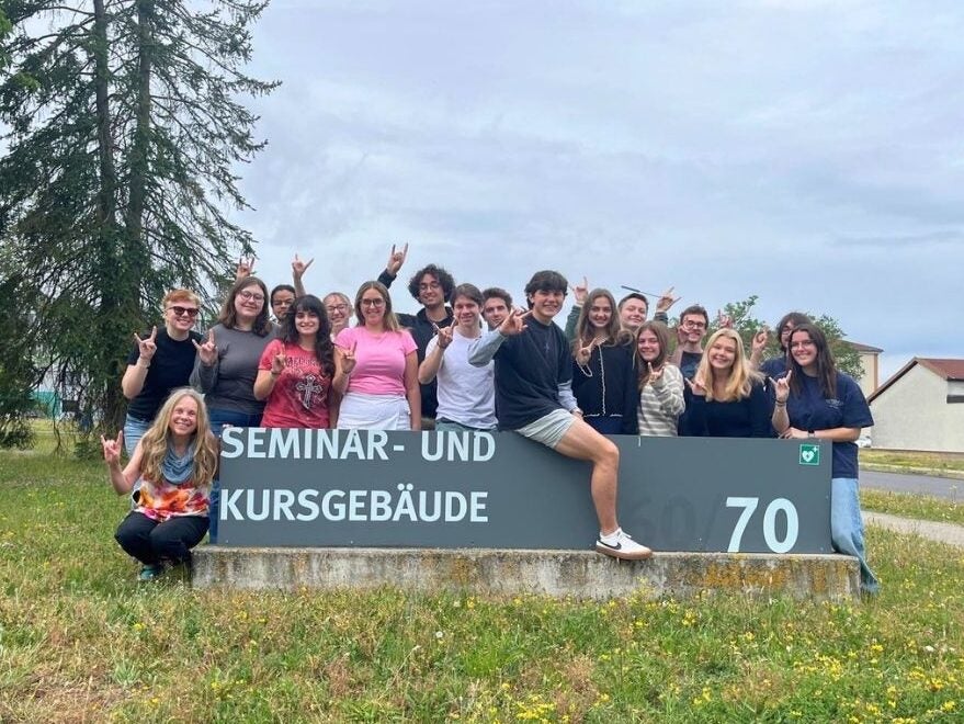 Group of young people posing happily around a Seminar and Course Building sign outdoors on a cloudy day.