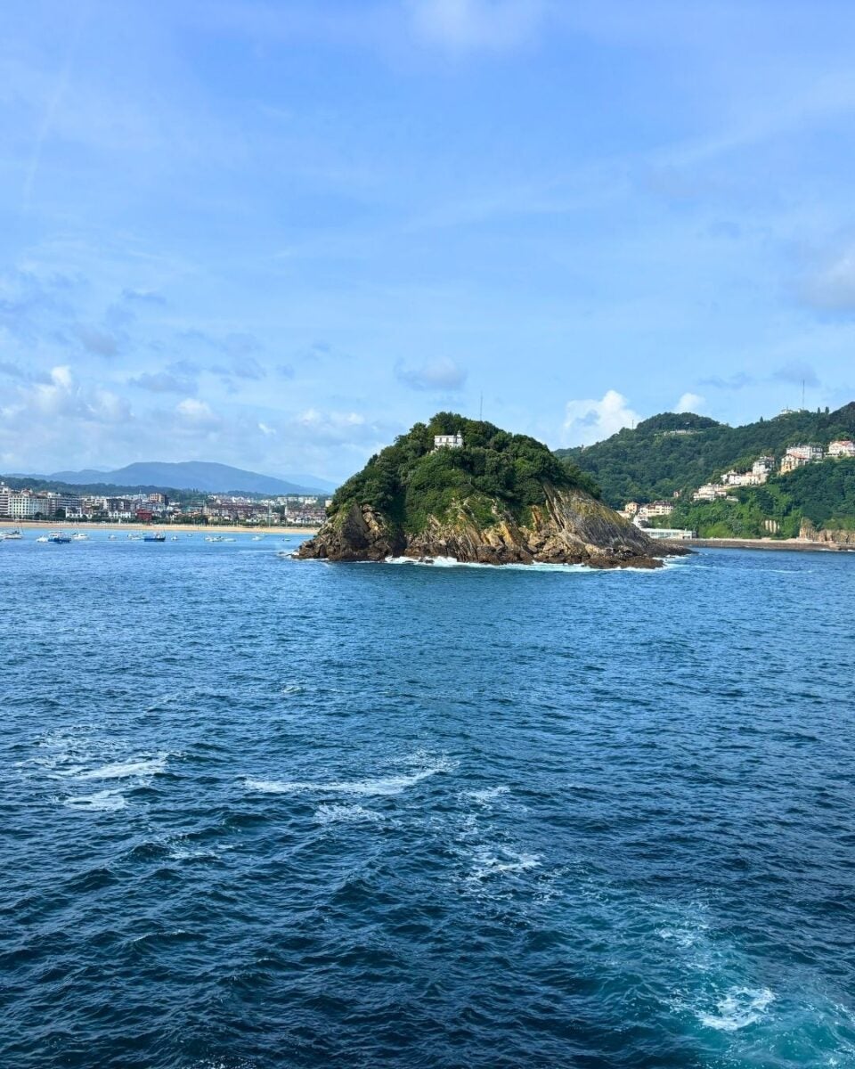 Small rocky island covered with greenery and a white building, surrounded by blue ocean waters under a partly cloudy sky.