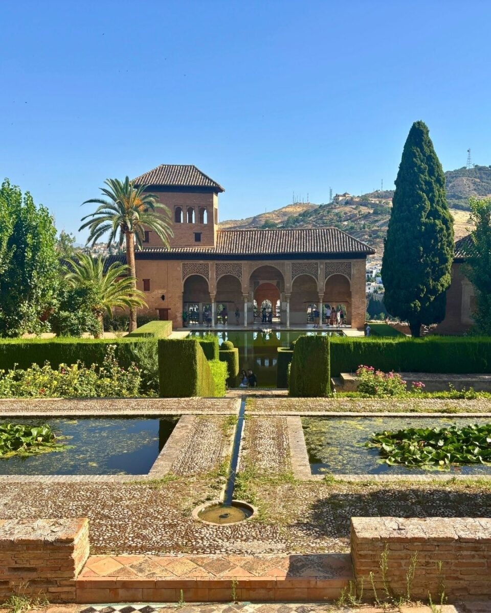 Historic Moorish palace with arched colonnades overlooking symmetrical reflecting pools and lush gardens under a clear blue sky.