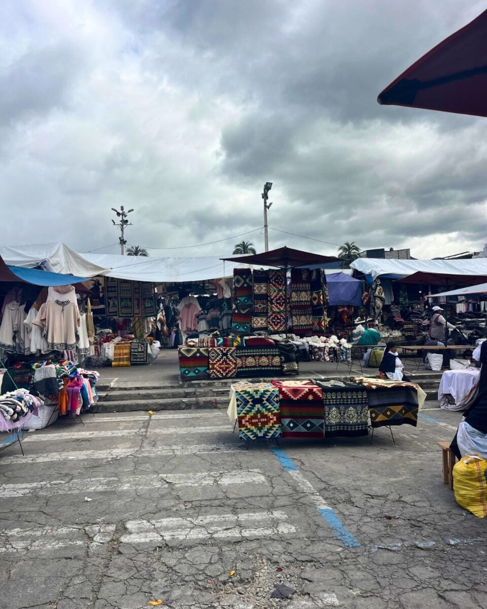 Outdoor market with colorful woven rugs and textiles displayed under cloudy skies.