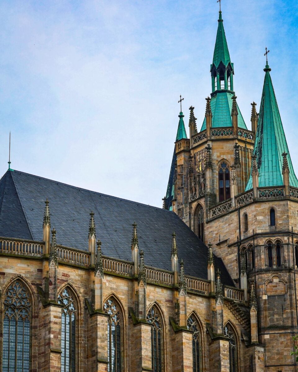 Gothic cathedral with tall green spires and detailed stone arches under a clear blue sky.