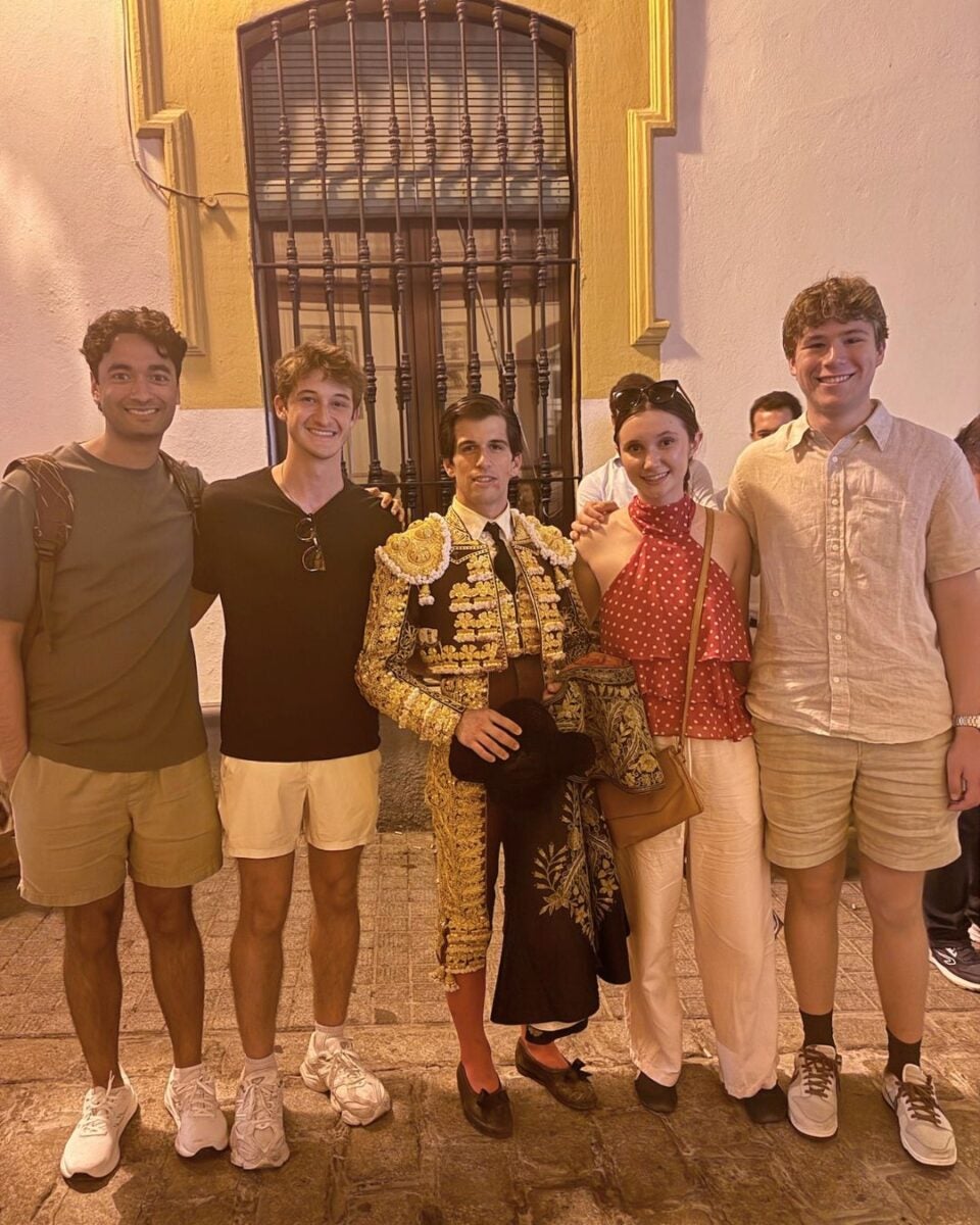 Group of five young adults posing together on a cobblestone street at night, with one dressed in a traditional ornate bullfighter costume.