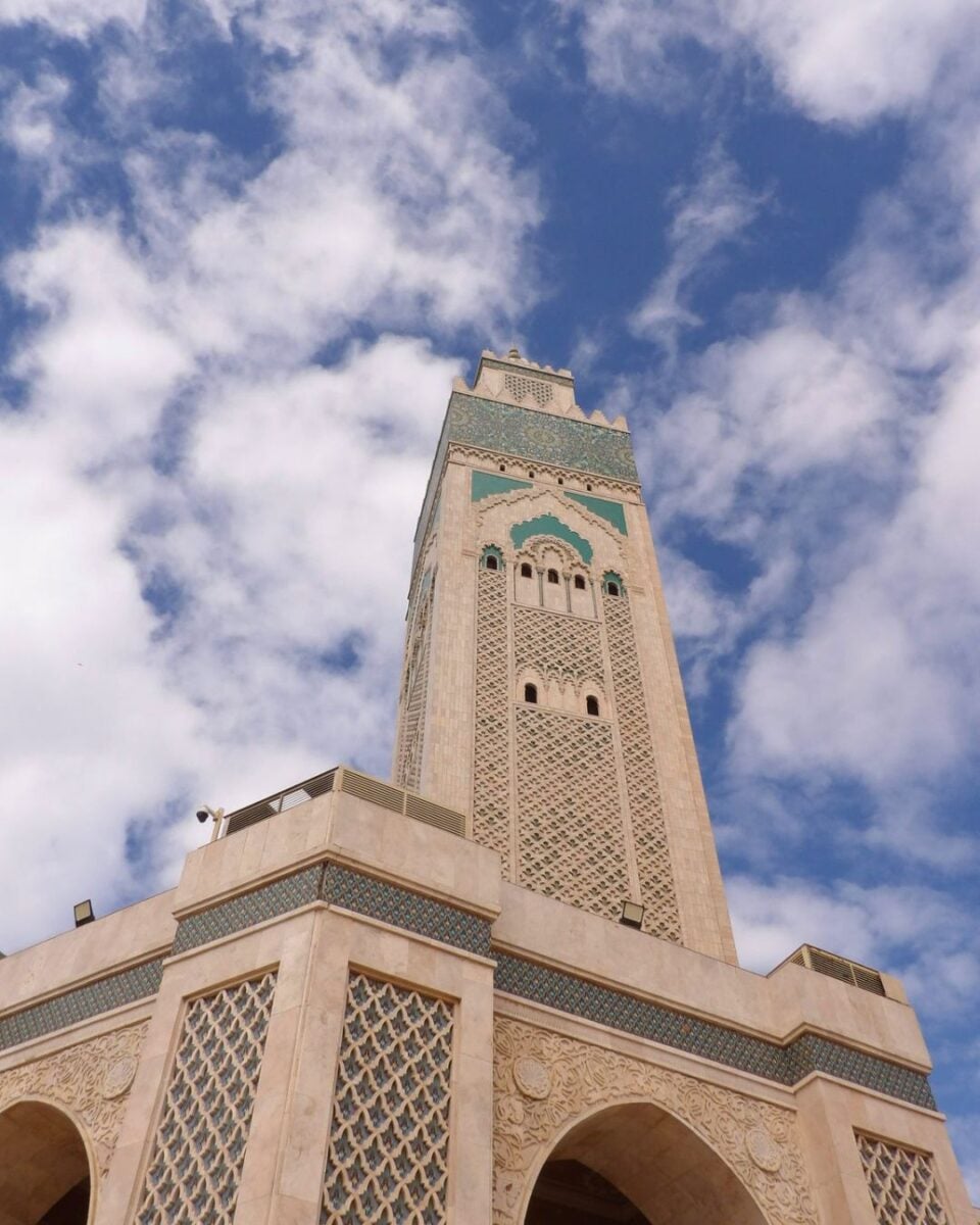 Tall ornate minaret with intricate geometric patterns against a partly cloudy blue sky.