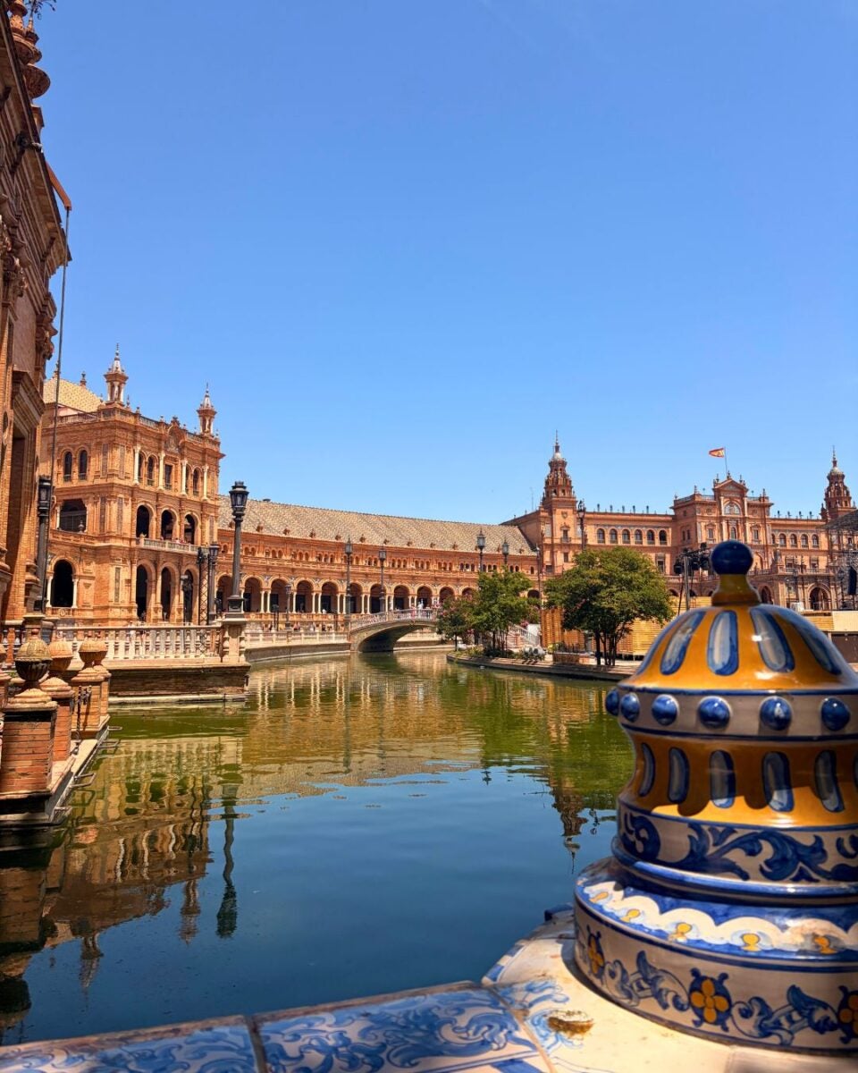 Ornate ceramic balustrade overlooking the calm canal and historic arches of Plaza de España in Seville under a clear blue sky.