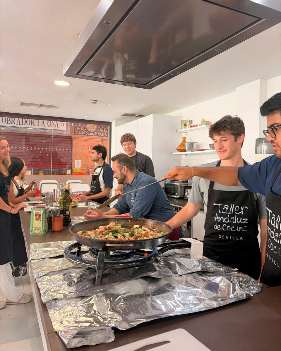 Group of young adults cooking paella together in a modern kitchen during a cooking class in Sevilla.