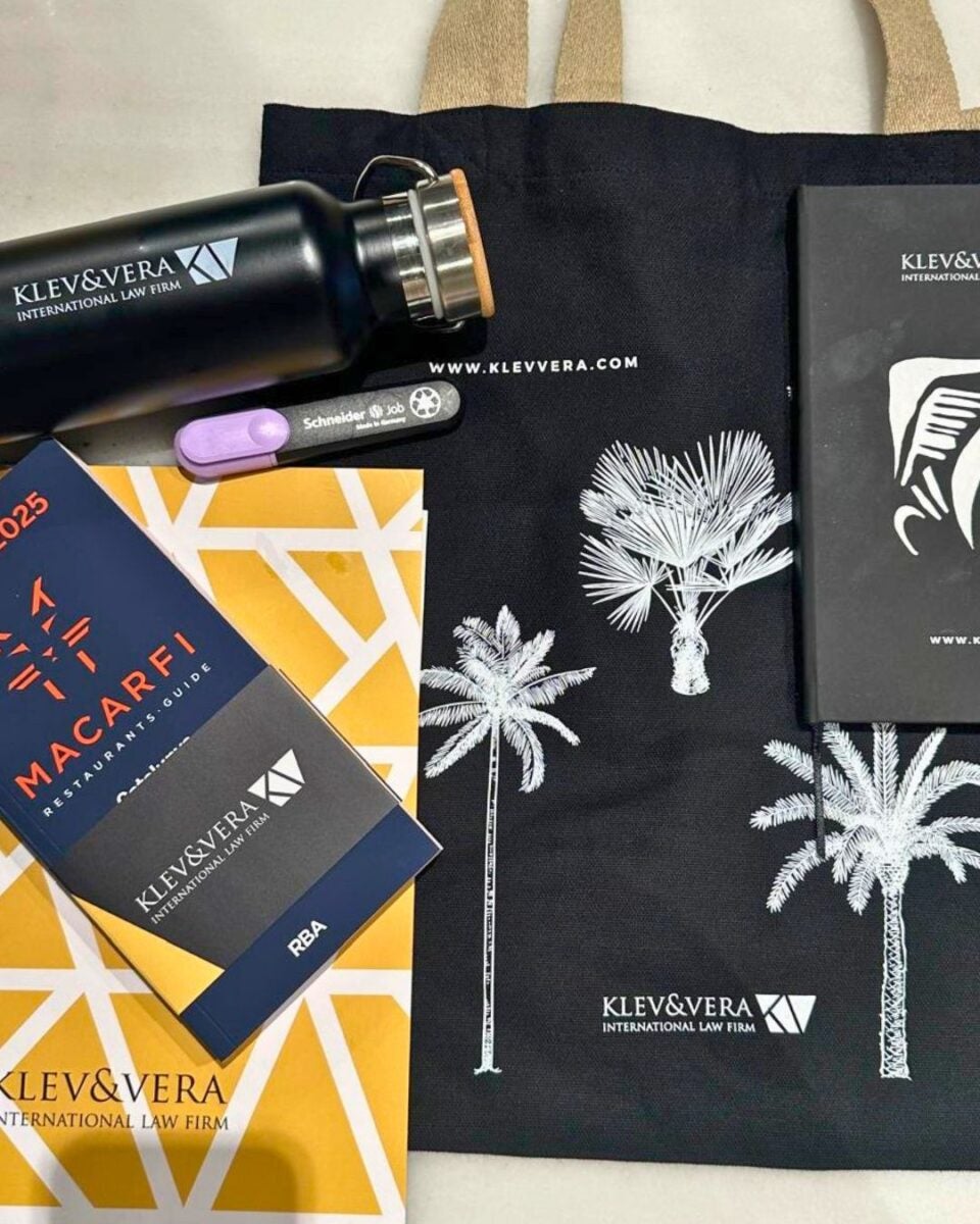 Black tote bag with white palm tree prints and Klev&Vera International Law Firm logo alongside branded water bottle, pen, and notebooks.
