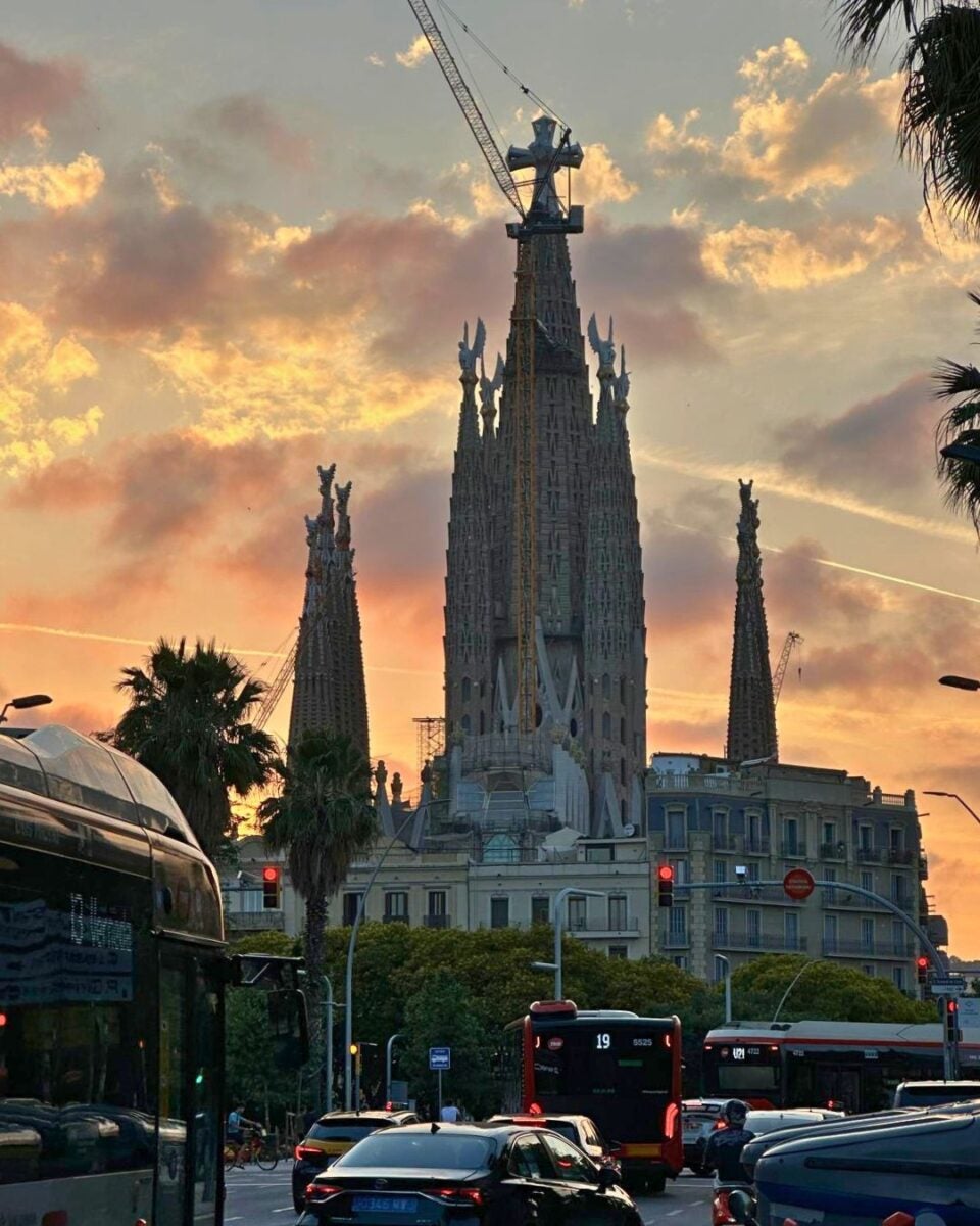 Sunset sky behind the towering spires of a Gothic-style cathedral with city traffic in the foreground.