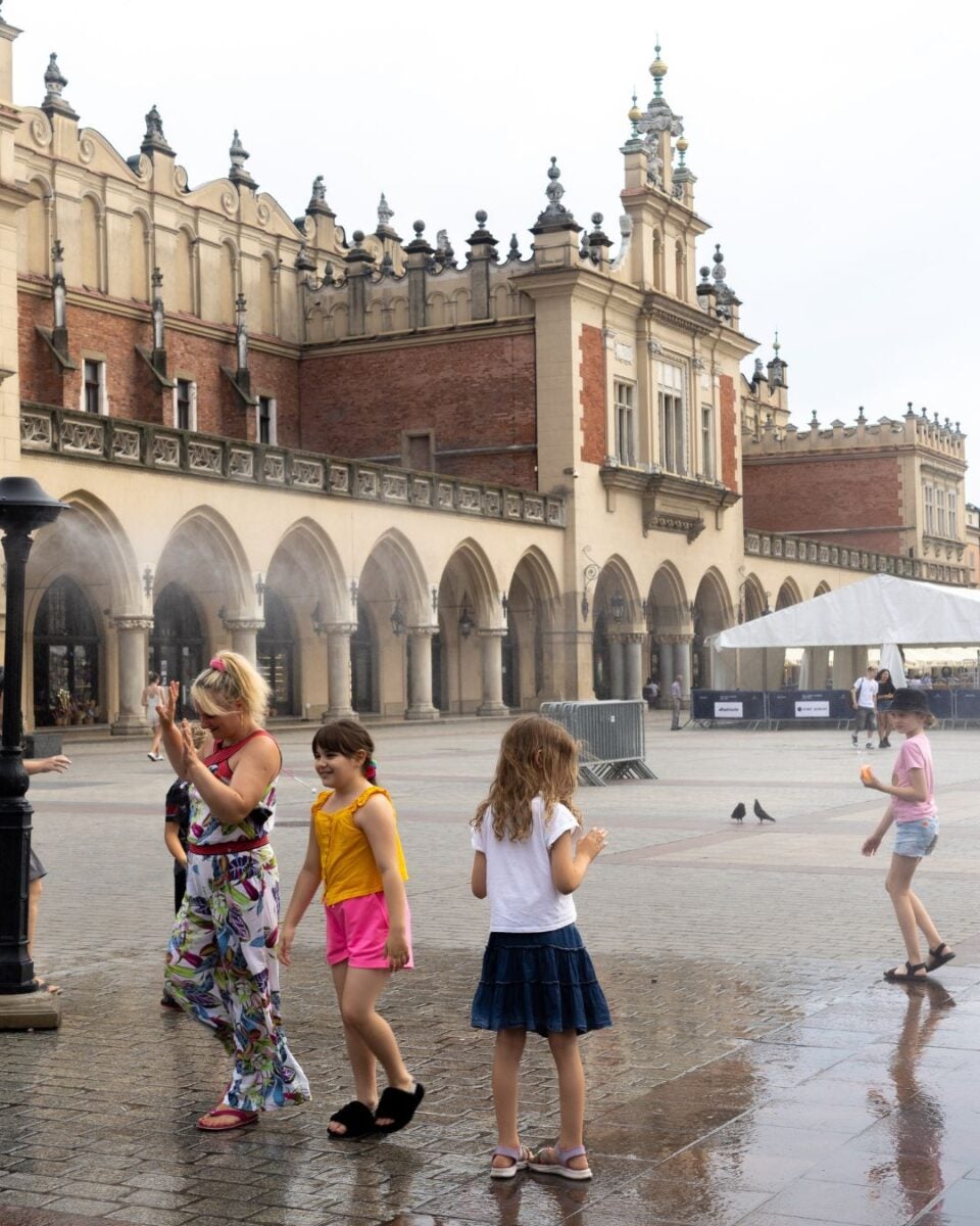 Children playing near a historic building with arched colonnades and ornate towers on a cloudy day.