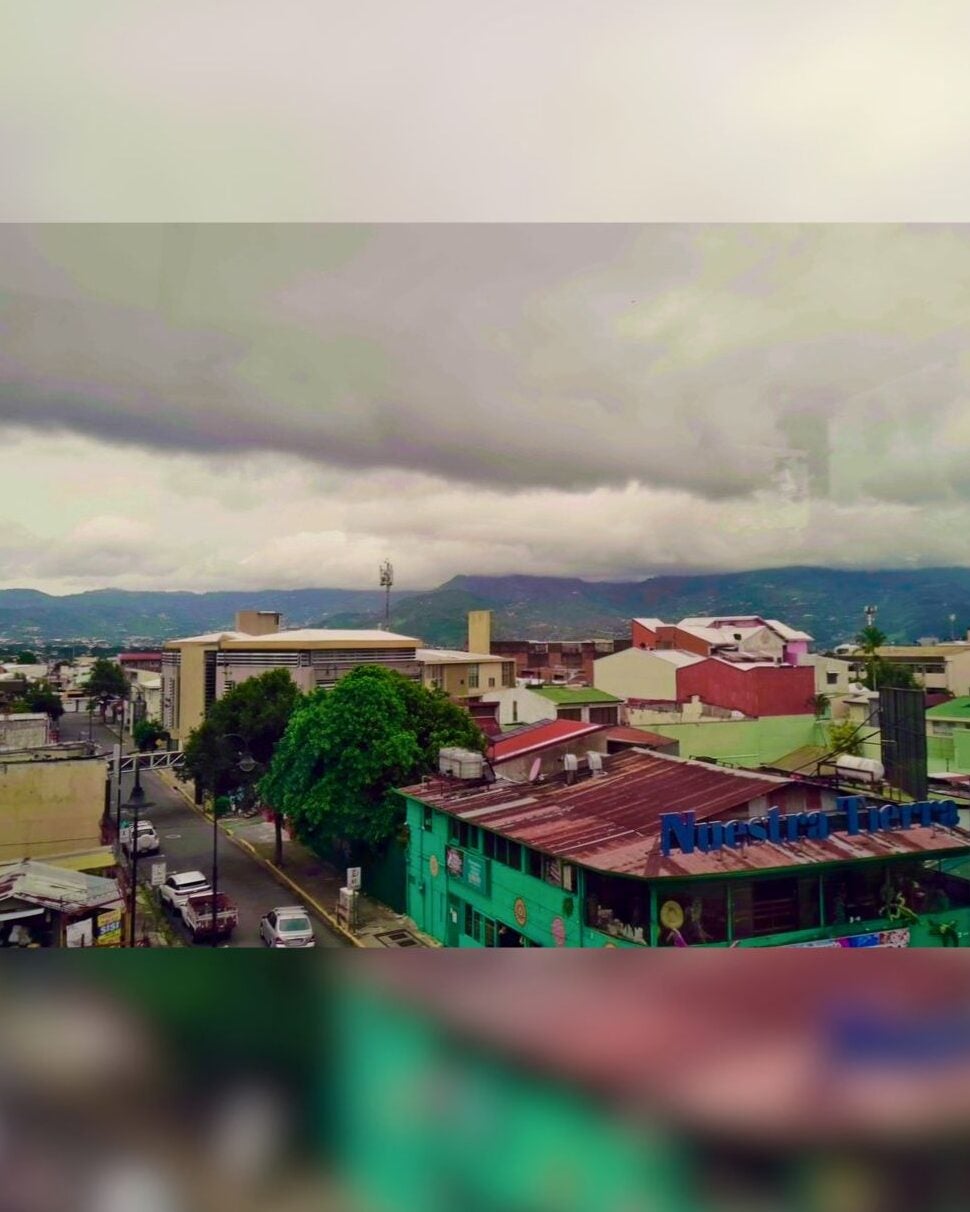 Overcast sky looms above a colorful urban neighborhood with green and red buildings and distant mountains.