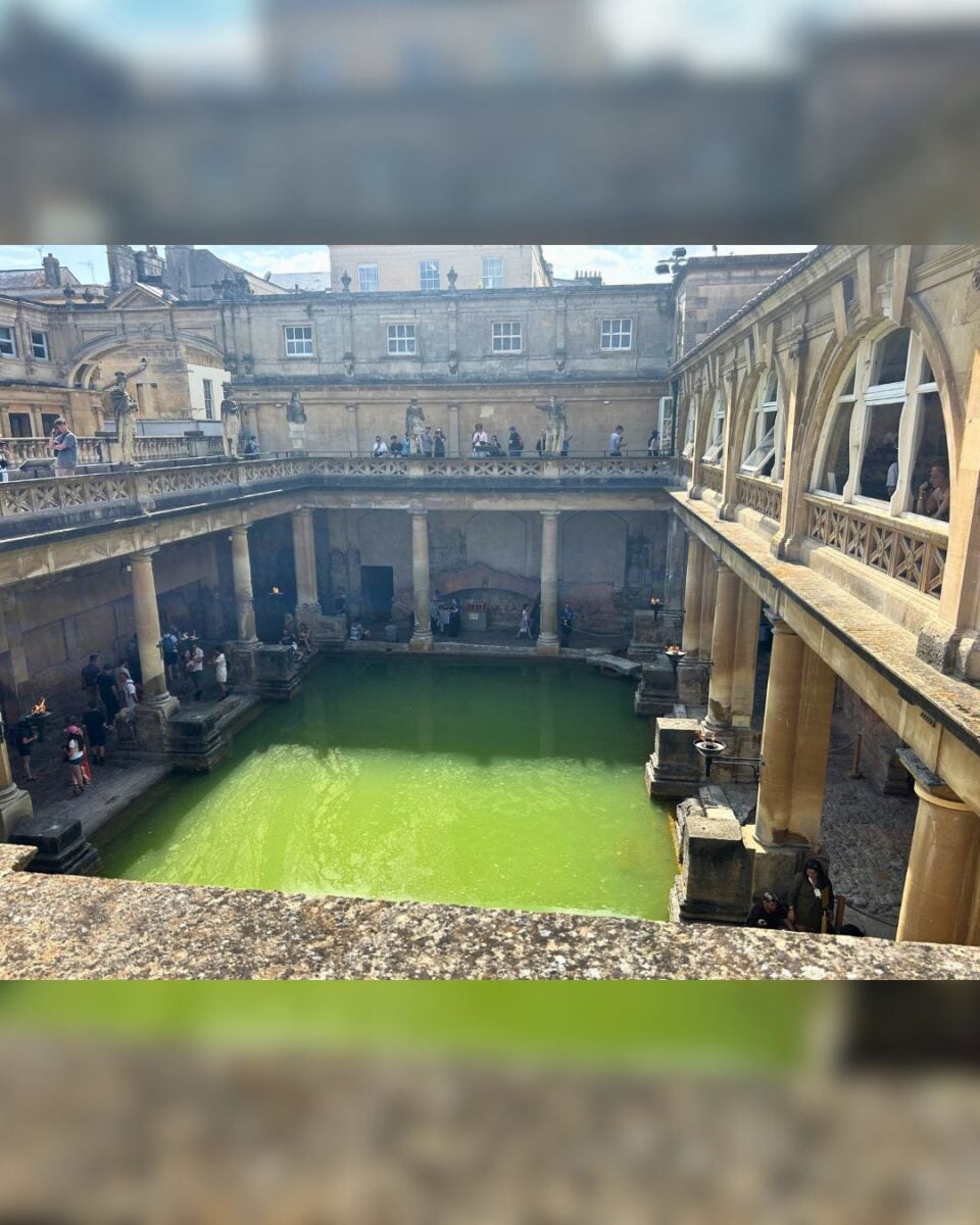 Ancient Roman-style public bath with green water surrounded by stone columns and historic architecture.