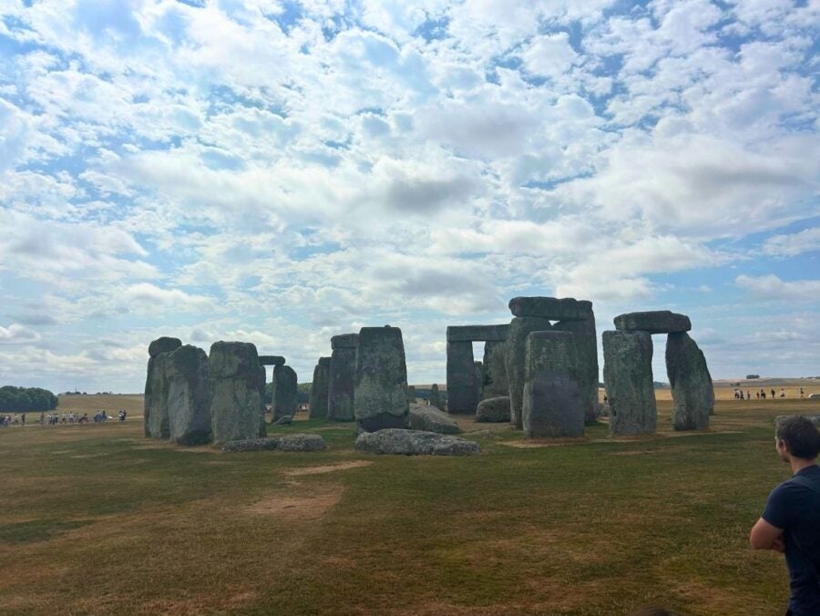 Wide view of Stonehenge's ancient stone circle under a partly cloudy sky on a grassy plain.