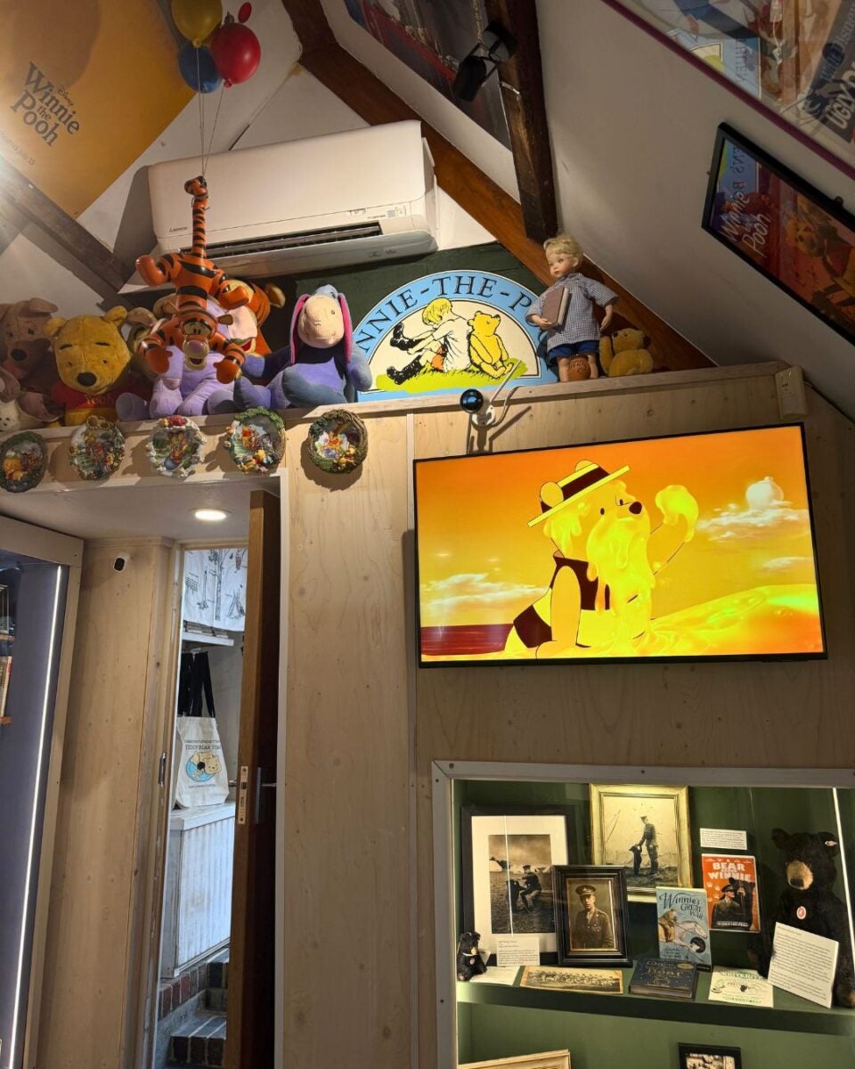 A cozy room corner decorated with Winnie the Pooh plush toys, a TV showing an animated scene, and framed photos and memorabilia below.
