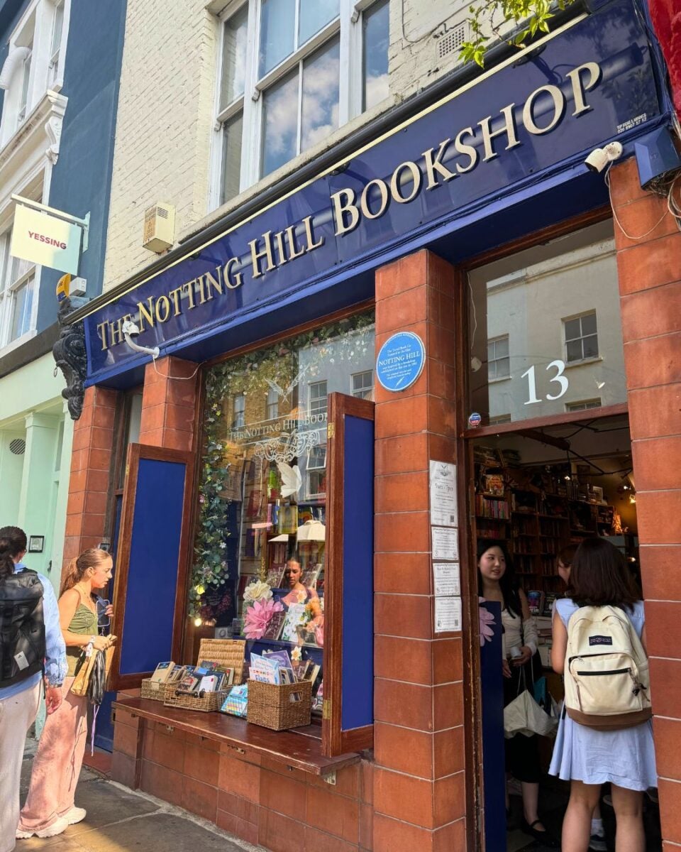 The exterior of The Notting Hill Bookshop with its blue sign and open doors showing people entering and browsing inside.
