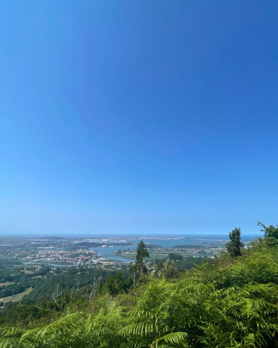 Panoramic view of a coastal town with waterways, surrounded by green hills under a clear blue sky.