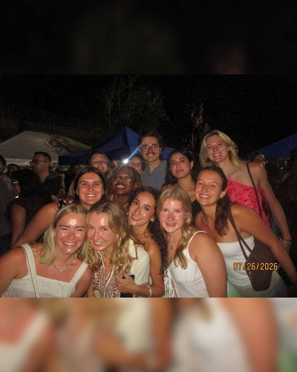 Group of friends smiling and posing closely together at an outdoor nighttime event with tents in the background.