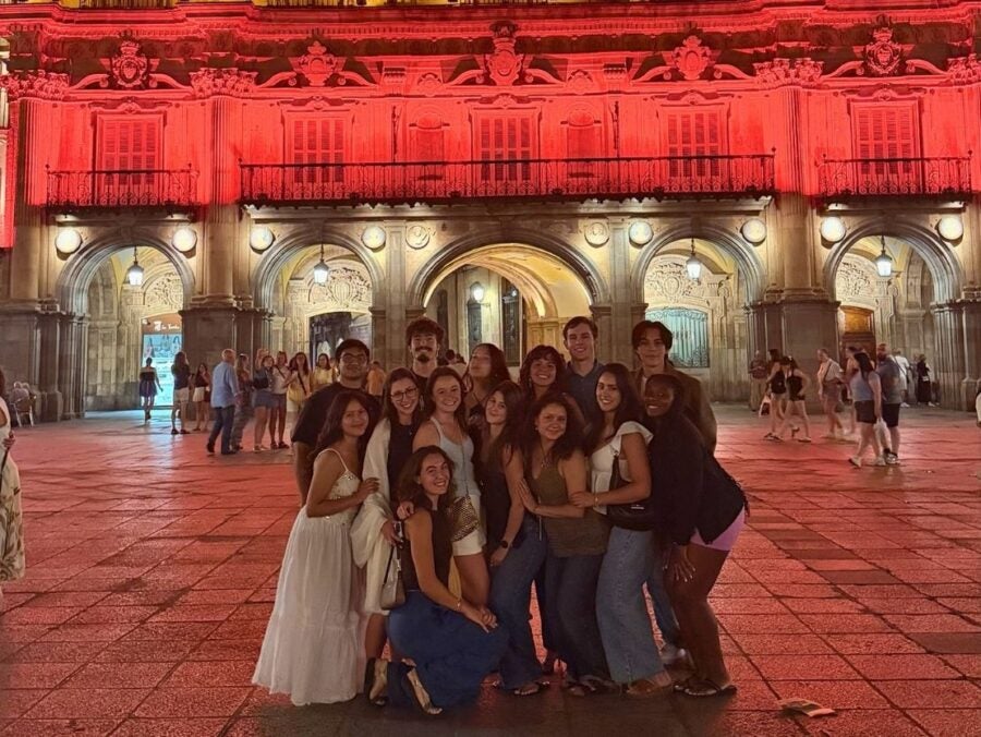 Group of friends posing together at night in a plaza with a historic building lit in red behind them.