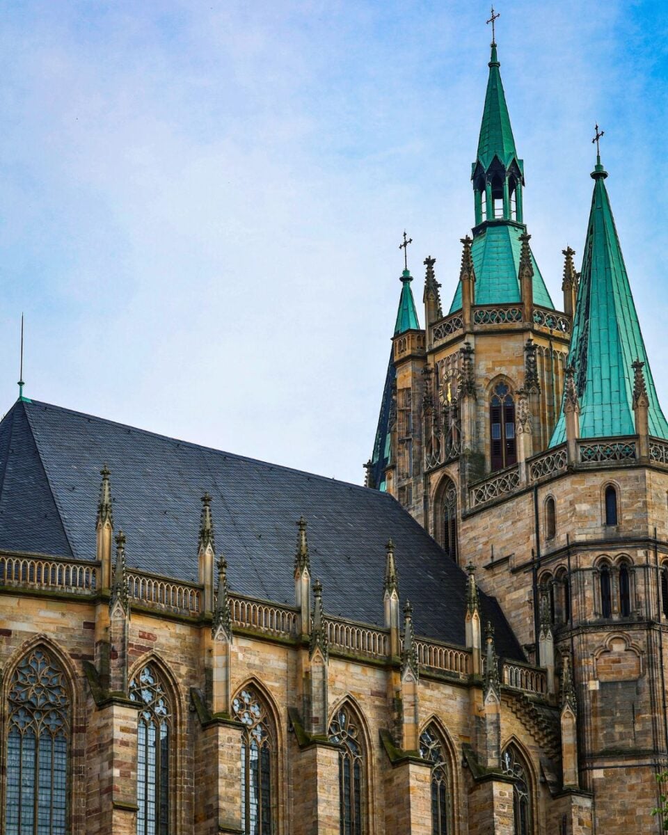 Gothic cathedral with tall green spires and detailed stonework under a clear blue sky.