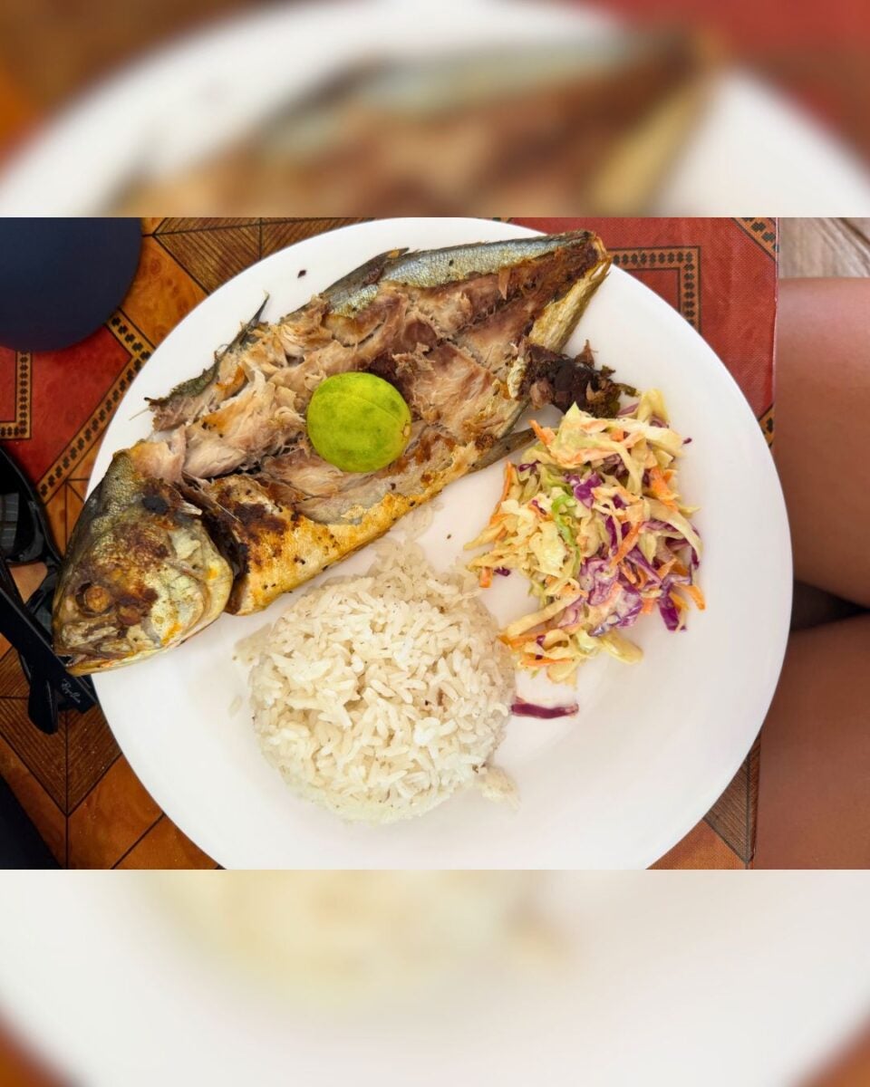 Grilled whole fish served with a lime wedge, white rice, and colorful coleslaw on a white plate.