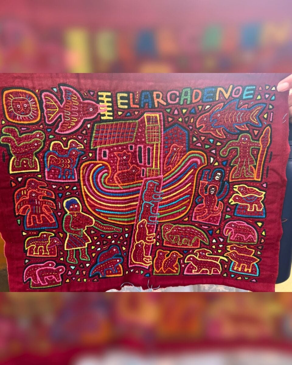 Colorful embroidered textile depicting Noah's Ark with animals and figures on a deep red background.