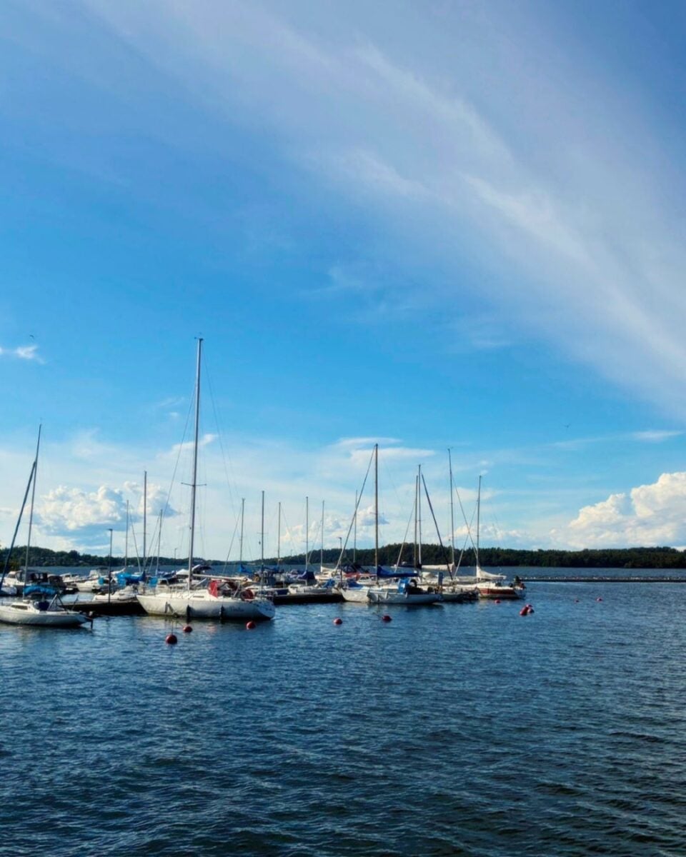 Sailboats moored in calm blue waters under a clear sky with scattered clouds on a sunny day.