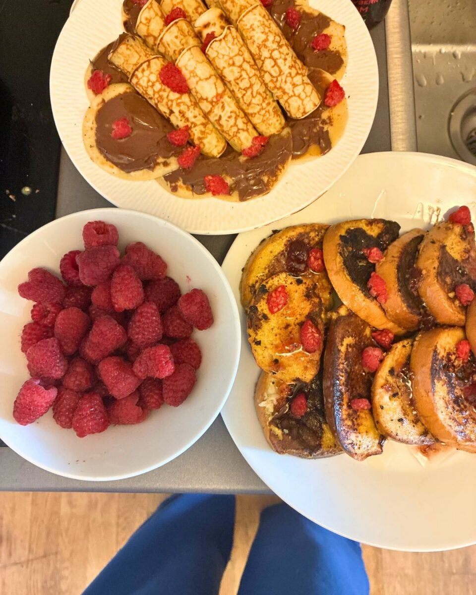 Plate of rolled crepes topped with chocolate spread and fresh raspberries beside a bowl of raspberries and a plate of toasted bread with chocolate and raspberries.