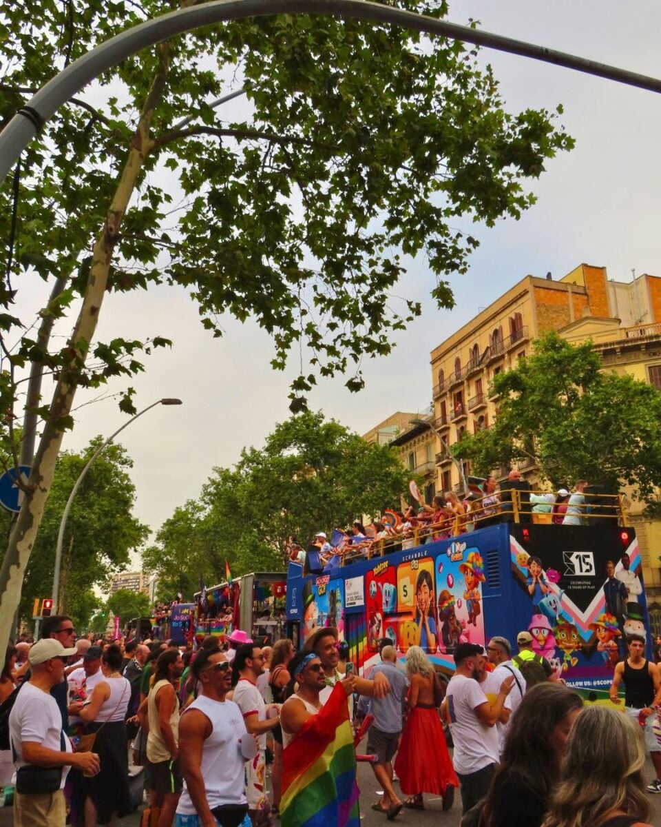 Crowd enjoying a colorful parade with decorated floats and people celebrating under leafy trees on a city street.